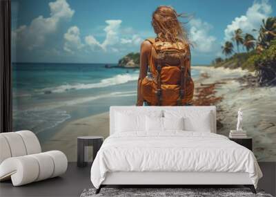 a solo female backpacker in casual attire walks on a sandy beach with a clear blue ocean and sky in  Wall mural