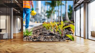 A worker in an urban environment with safety hat and vest tends to young plants in a vibrantly green setting, symbolizing the intersection of industry and nature. Wall mural