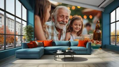 Smiling senior man at a table with his laughing grandchildren enjoying a family meal outdoor Wall mural