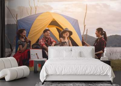 Group of man and woman enjoy camping picnic and barbecue at lake with tents in background. Young mixed race Asian woman and man. Young people's hands toasting and cheering bottles of beer.  Wall mural