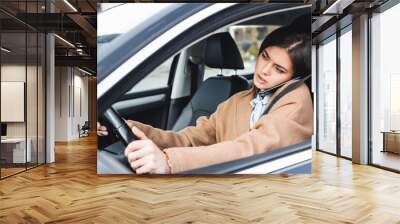  woman in autumn outfit driving car and talking on mobile phone on blurred foreground Wall mural