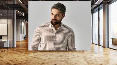 A bearded man in an elegant striped shirt strikes a pose against a grey studio background. Wall mural