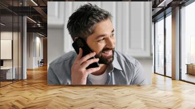 A bearded man in casual attire smiling while talking on his phone. Wall mural