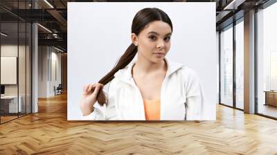 A brunette teenage girl with a ponytail wearing sportive attire against a grey studio backdrop. Wall mural