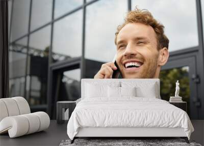 A cheerful businessman with red hair discusses a project on his phone while in a sleek office. Wall mural