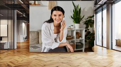 A chic woman in casual attire chats on her cell phone while working at home. Wall mural