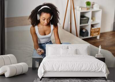 A curly African American woman in a tank top sits on a bed, using a laptop computer in a modern bedroom. Wall mural