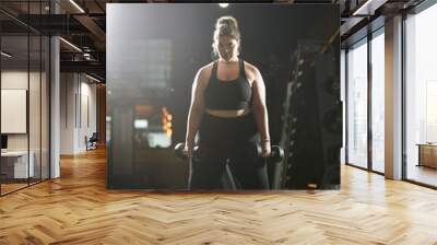 A determined young woman embraces her strength while working out in stylish active wear at the gym. Wall mural