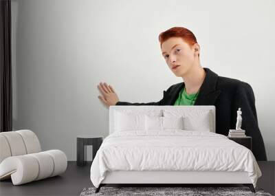 A fashionable young man with striking red hair showcases an elegant coat and a casual shirt in a studio. Wall mural