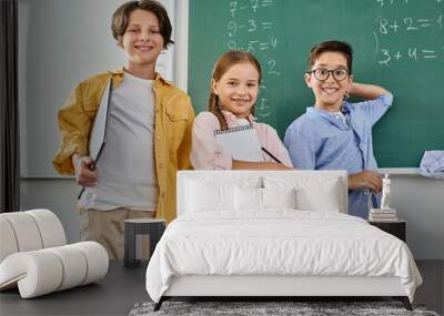 A group of children stand attentively in front of a chalkboard in a bright, lively classroom. Wall mural