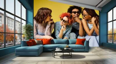 A group of young multicultural friends, including a nonbinary person, sitting closely together in stylish attire in a studio setting. Wall mural