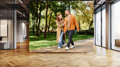 A man and woman in casual attire walk down a peaceful path in a lush park. Wall mural