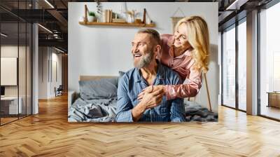 A man carrying a woman on his back in a cozy bedroom setting, showing love and unity in their relationship. Wall mural