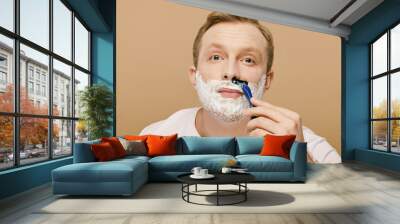 A man in casual attire carefully shaving his face with a razor. Wall mural