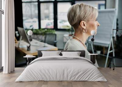 A middle-aged businesswoman with short hair immersed in work at a modern office desk. Wall mural