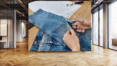 A person reinvents old jeans with scissors. Wall mural