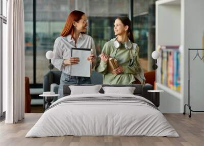 A redhead woman teaches a teenage girl in a library, both engrossed in after-school lessons Wall mural