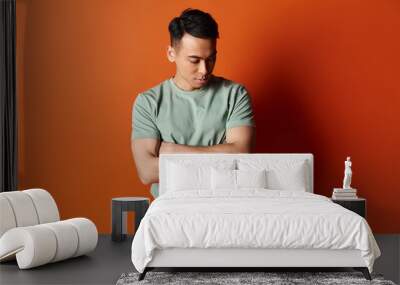 A stylish Asian man in fashionable attire stands confidently against a vibrant orange wall in a studio. Wall mural