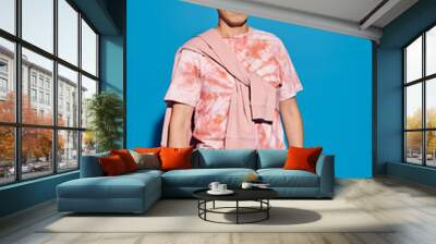 A stylish young man strikes a pose in front of a vivid blue wall, exuding confidence and charisma. Wall mural