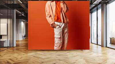 A trendy, emotional young African American man stands confidently against a bright orange background in fashionable attire and sunglasses. Wall mural