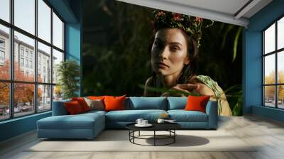 A woman adorned with a floral crown poses in a swamp, surrounded by lush greenery. Wall mural