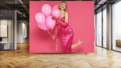 A woman in a pink dress smiles as she holds a bunch of pink balloons. Wall mural