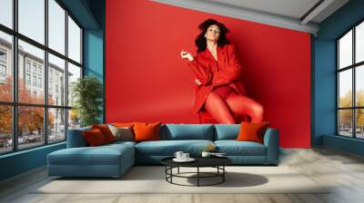 A young woman in a striking red coat and tights poses on a vibrant background in a studio setting. Wall mural