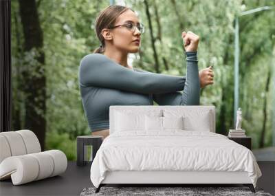 A young woman in sportswear stretches outdoors, embracing fitness and nature Wall mural