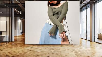 A young woman with brunette hair strikes a stylish pose in a studio while wearing a skirt and sunglasses. Wall mural