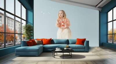 adorable kid in faux fur coat and skirt sitting on highchair and blowing soap bubbles isolated on grey Wall mural