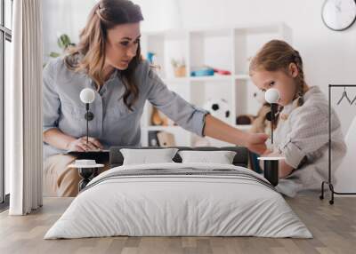 adult psychologist with clipboard talking to sad little child in office Wall mural