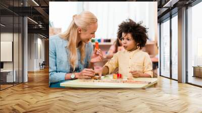 African american child playing educational game with smiling teacher in montessori school Wall mural