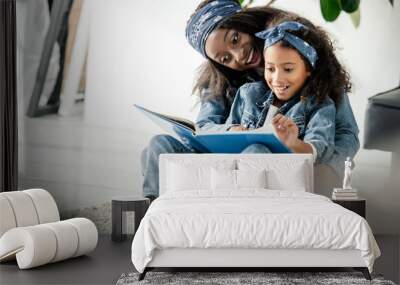 african american mother and smiling daughter looking at family photo album at home Wall mural