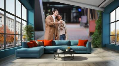 african american woman holding shopping bags near happy boyfriend in coat in mall. Wall mural