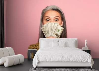 amazed middle aged woman covering face with dollar banknotes isolated on pink Wall mural