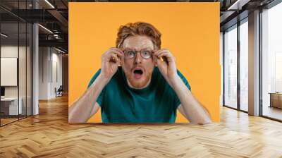 Amazed redhead man adjusting glasses isolated on yellow Wall mural