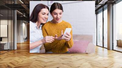 amazed teenage girl looking at smartphone near mother Wall mural