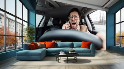 angry man talking on smartphone while driving car on blurred foreground Wall mural