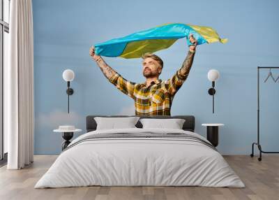 appealing Ukrainian man in casual attire posing with national flag, scenic landscape, modern farmer Wall mural