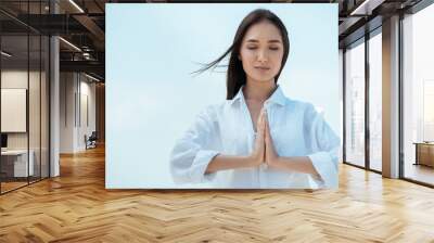 asian woman with closed eyes doing namaste mudra gesture against blue sky Wall mural