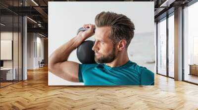 athletic man looking away while exercising with kettlebell at home Wall mural