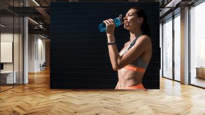 athletic woman with fitness tracker drinking water from sports bottle Wall mural