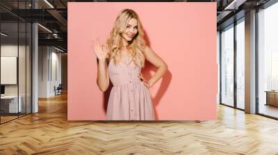 attractive and blonde woman in pink dress with hand on hip showing okay Wall mural