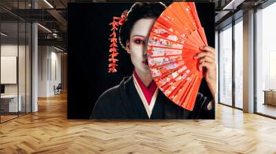 attractive geisha in black kimono with flowers in hair holding bright hand fan isolated on black Wall mural