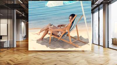 attractive girl in bikini with coconut cocktail resting on beach under umbrella Wall mural