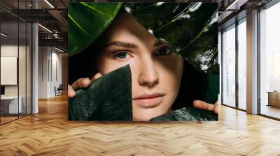 attractive girl with freckles on face posing with tropical leaves isolated on green Wall mural