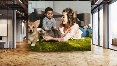 attractive woman and little boy laying on floor with dog and cat in living room at home Wall mural