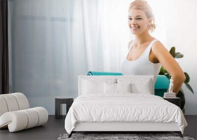 attractive woman smiling and holding fitness mat in living room Wall mural