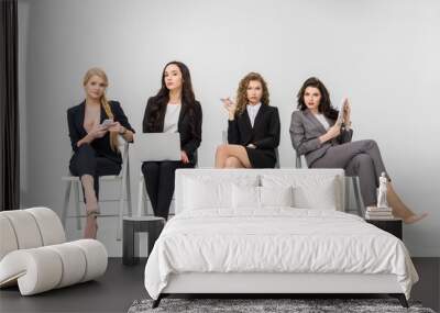 attractive women in formal wear sitting on chairs and using gadgets isolated on grey Wall mural