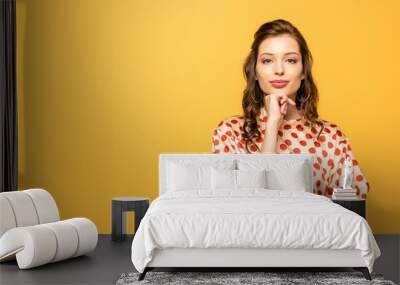 attractive young woman holding hand near chin while smiling at camera isolated on yellow Wall mural